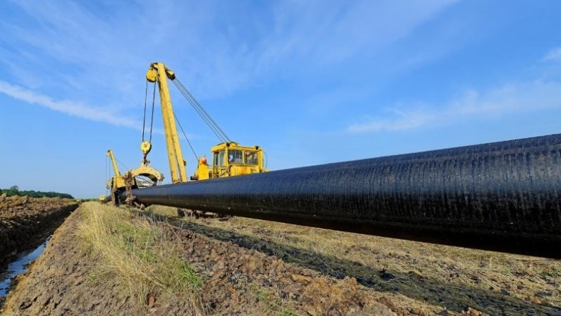 Large steel pipeline being installed in open field using crane