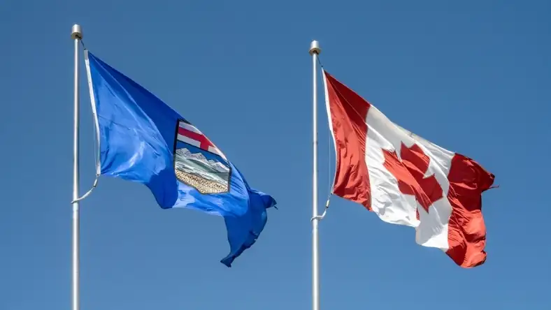 Flags of Alberta and Canada wave in the wind against a bright blue sky