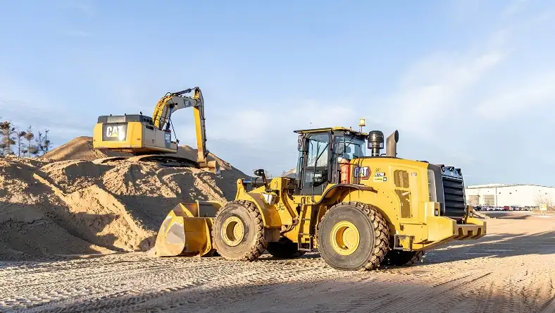 Yellow CAT wheel loader and excavator moving a large frac sand stockpile at an outdoor industrial site