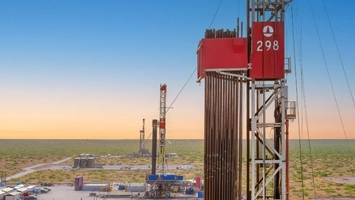 Two oil drilling rigs on a flat arid plain at dusk, with a red-branded derrick numbered 298 in the foreground