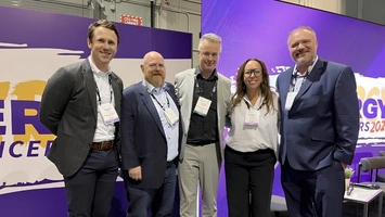 Five professionals stand together at a trade show booth during an industry conference
